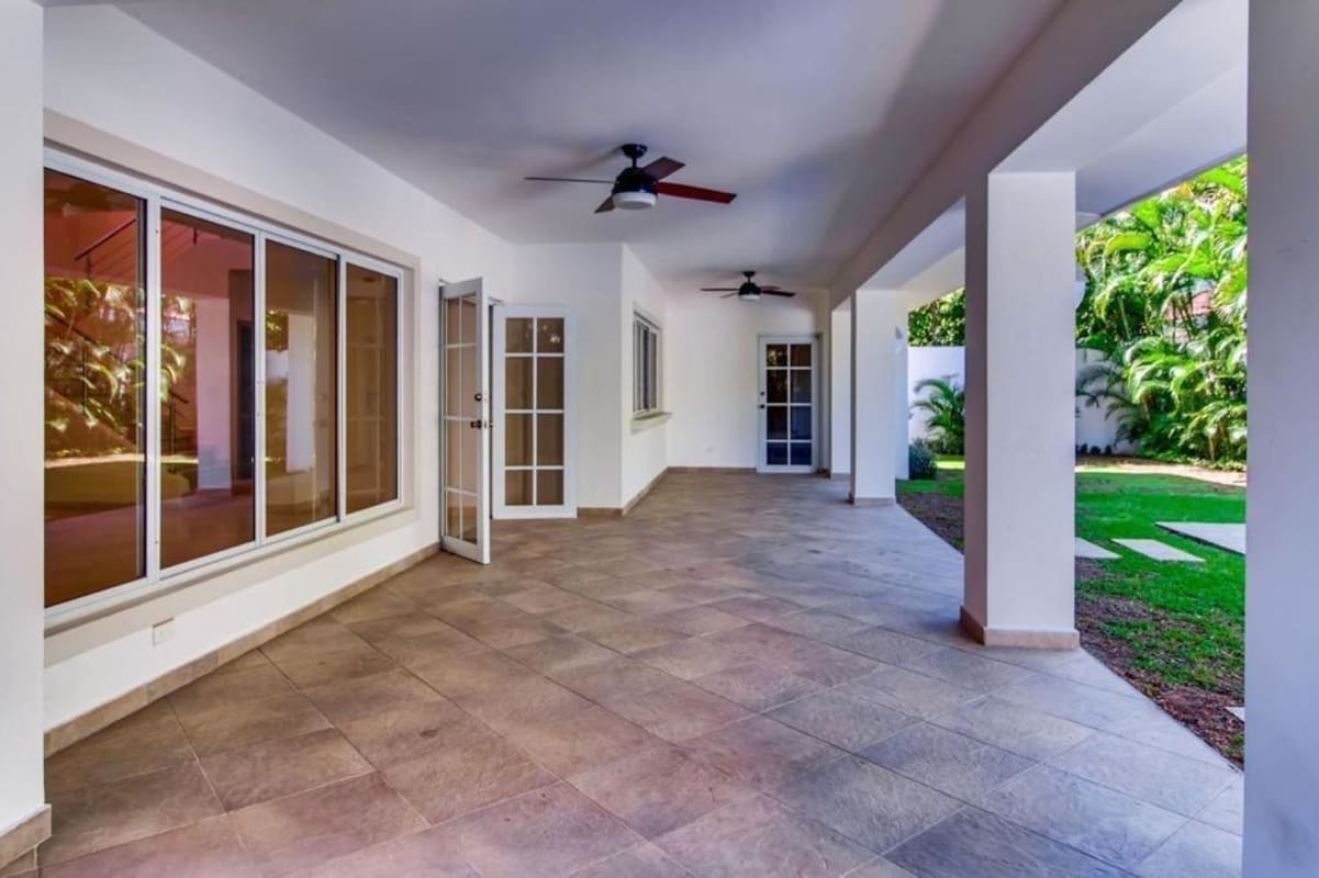 Spacious covered patio area with ceiling fans, glass sliding doors, overlooking green garden and pool in Costa del Este Panama