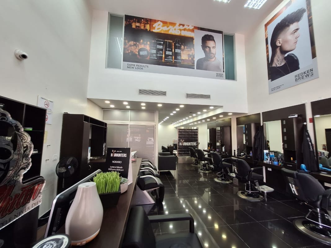 Large commercial barbershop with double height ceiling, barber chairs, product posters Costa del Este