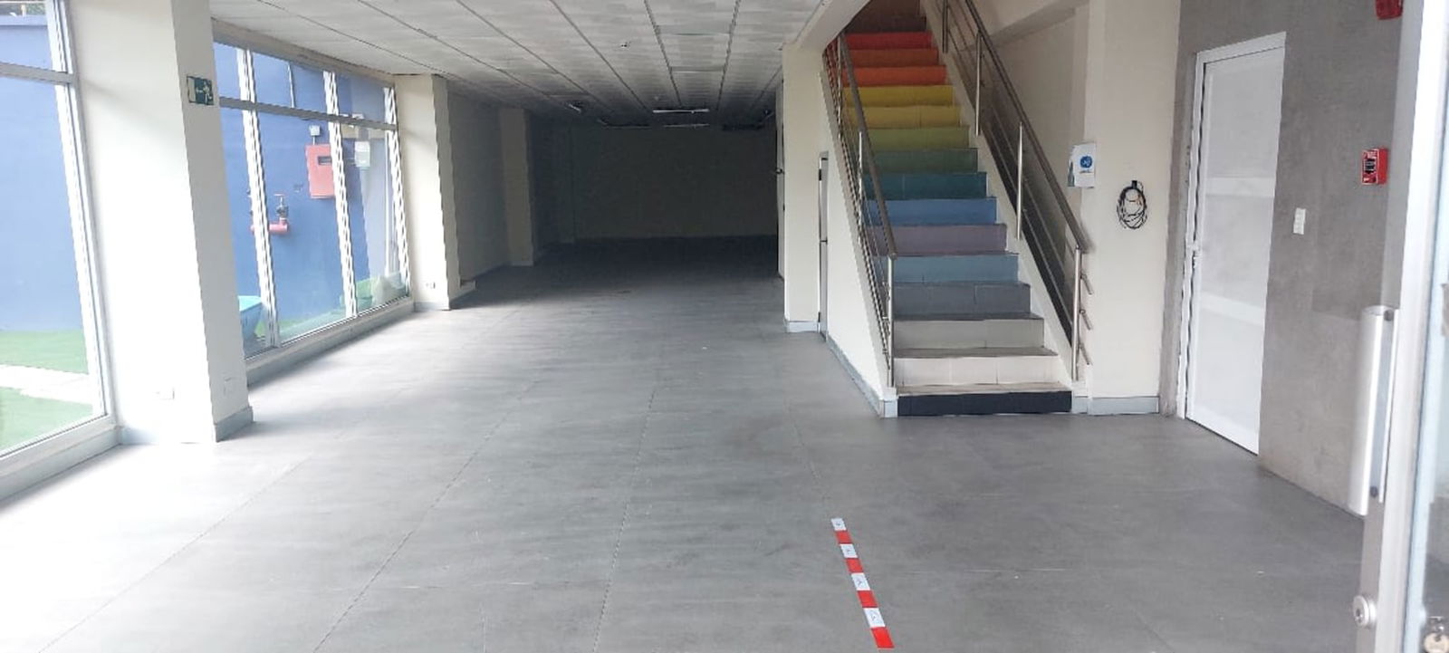 Large commercial interior with floor-to-ceiling windows and rainbow staircase Chanis Panama City