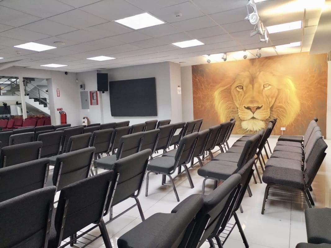 Large meeting or auditorium room with lion mural, stacked chairs, and lighting for commercial or church use