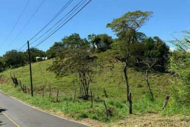Green hillside lot with fence and paved country road access in Boquete Panama