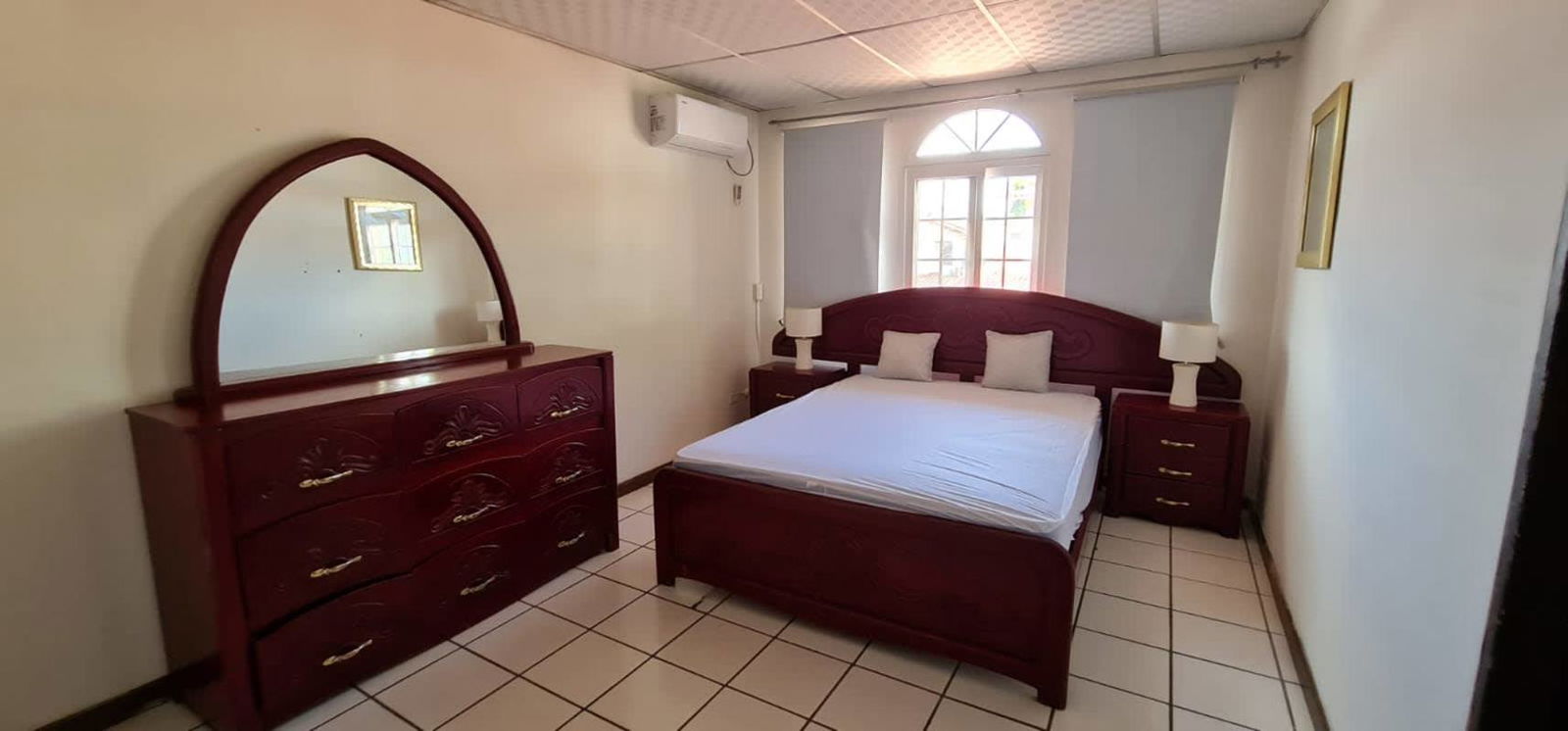 Bedroom with wood furniture, arched window, split AC unit in gated furnished house Panama City