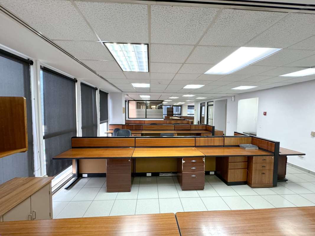 Office area with multiple wooden desks, tiled floor, ceiling lights in PH Humbold Panama City