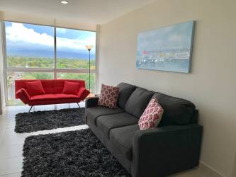Modern living area with large windows, red sofa, panoramic view in PH Ibiza Coronado Beach apartment Panama