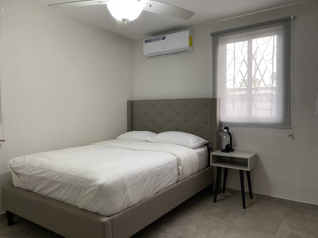 Bedroom with gray tufted bed, AC unit, ceiling fan furnished rental in Don Bosco Panama
