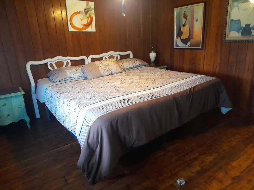 Rustic bedroom with framed artwork and wooden walls in Cerro Azul mountain house Panama