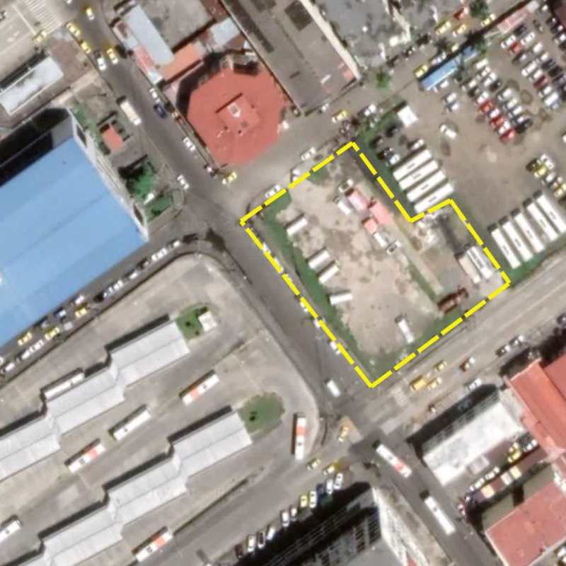 Aerial shot marking vacant commercial plot outlined in yellow near city center, surrounded by roads and buildings