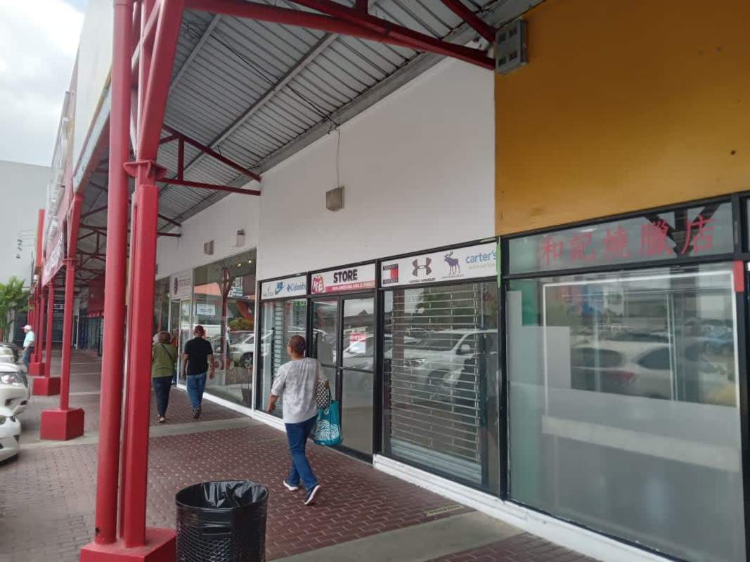 Covered exterior walkway with glass storefronts and parking lot in Los Pueblos Panama City