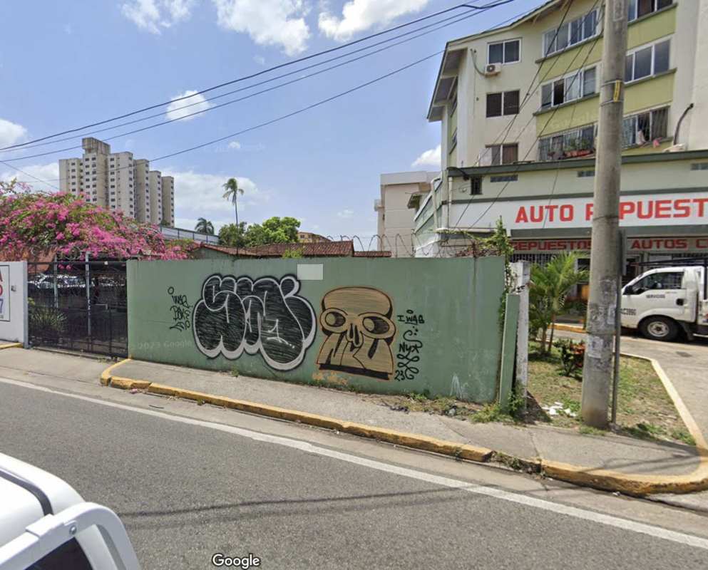 Urban street with retail stores, graffiti wall, and truck in front of commercial lot for sale on Via Cincuentenario Panama City