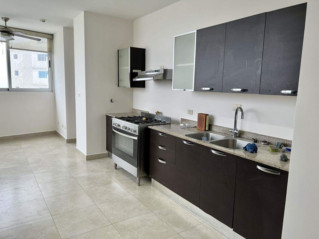 Modern kitchen with dark cabinets, granite countertops, double sink, and large window at PH Pearl Costa del Este Panama
