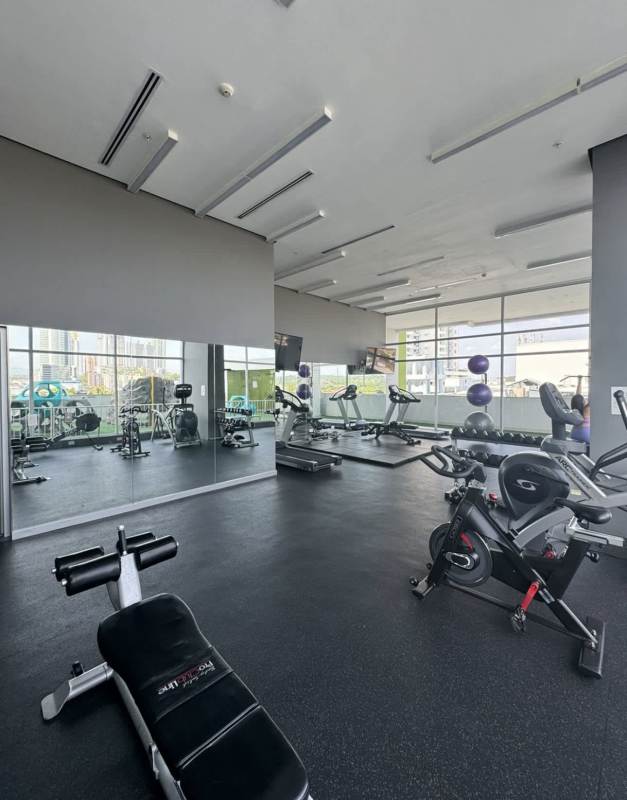 Modern gym equipped with machines and city view windows PH Vivendi Green Panama City
