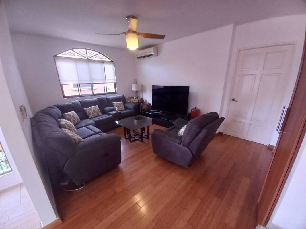 Living room with gray sectional, TV, wooden floors, ceiling fan Clayton Village Panama