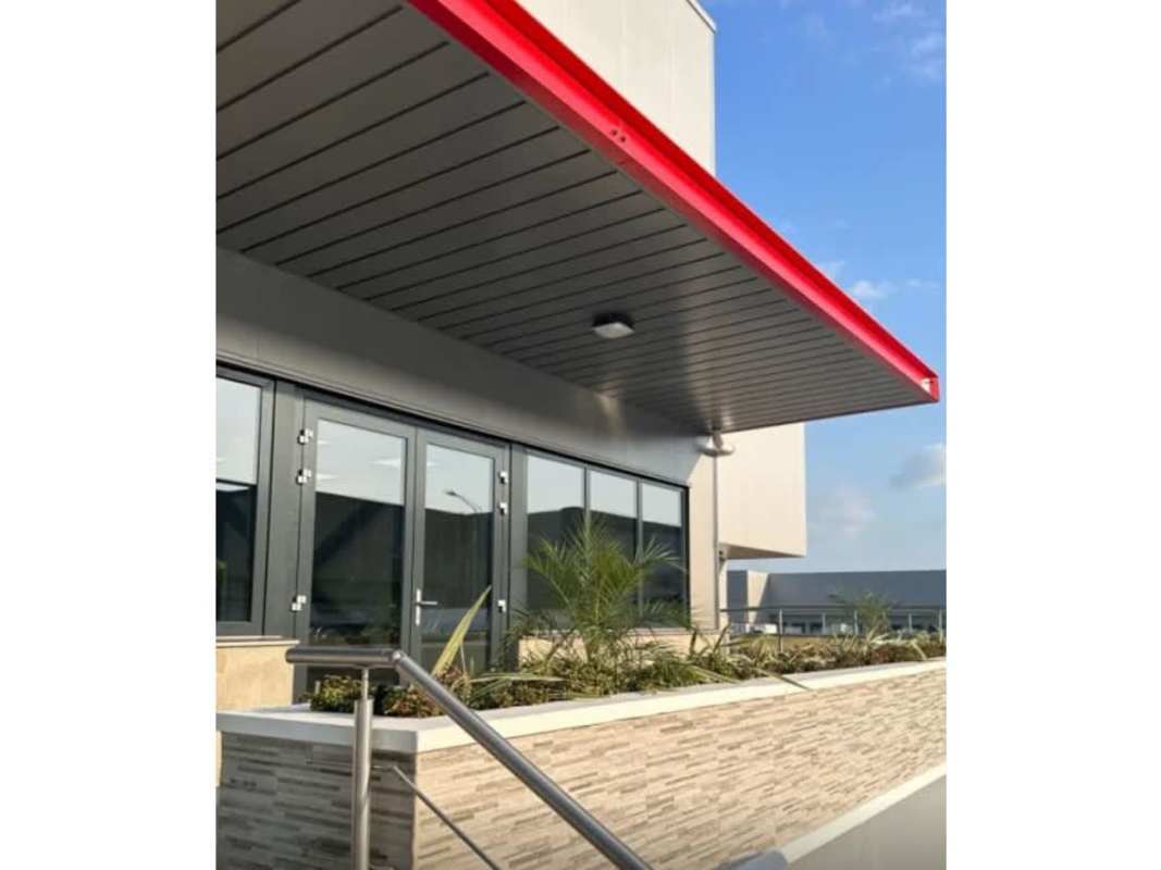 Gray industrial canopy with red trim large glass entrance doors and planter Panama warehouse