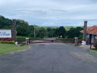 Stone pillar gate entrance with security booth, wooden gate and lush greenery at El Valle Village in Panama