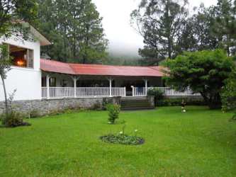 Exterior view of single story traditional ranch style house with red metal roof and large lawn in Boquete Panama