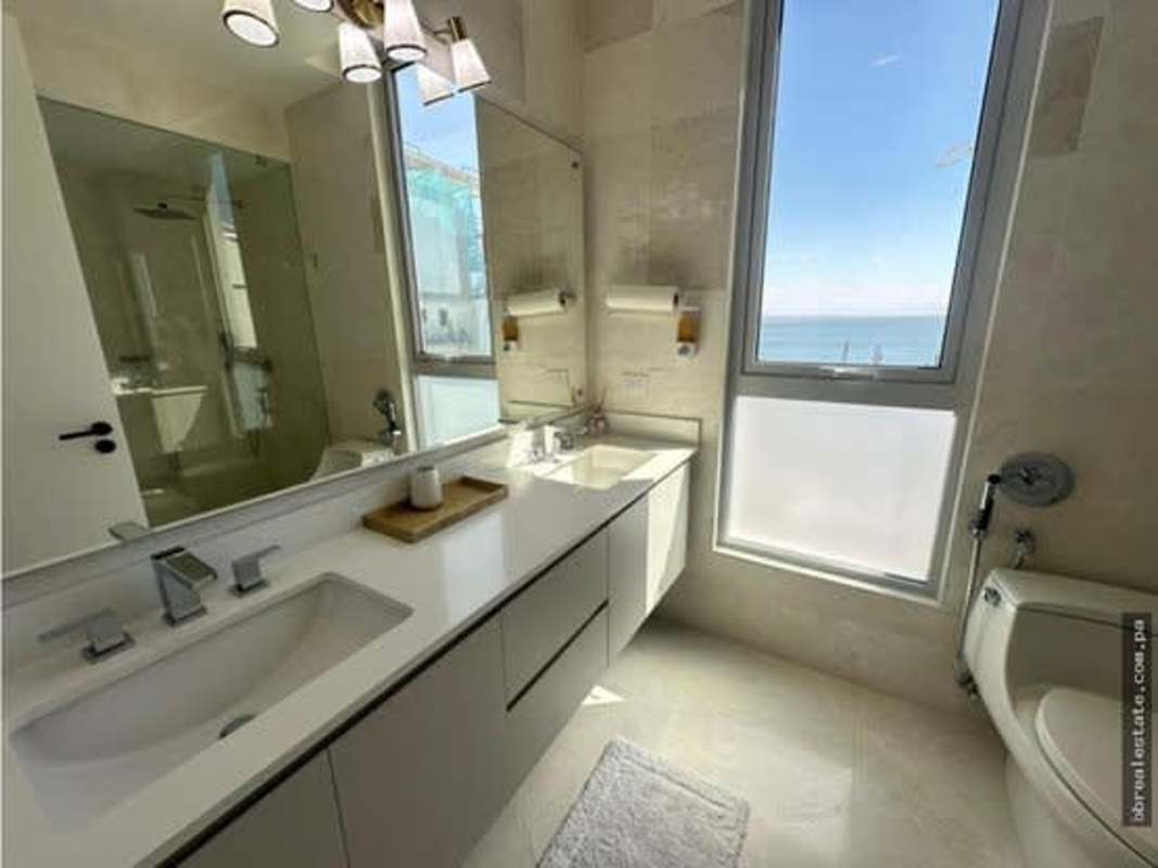 Modern bathroom with double vanity sinks, glass shower, large mirror and oceanfront window in luxury condo