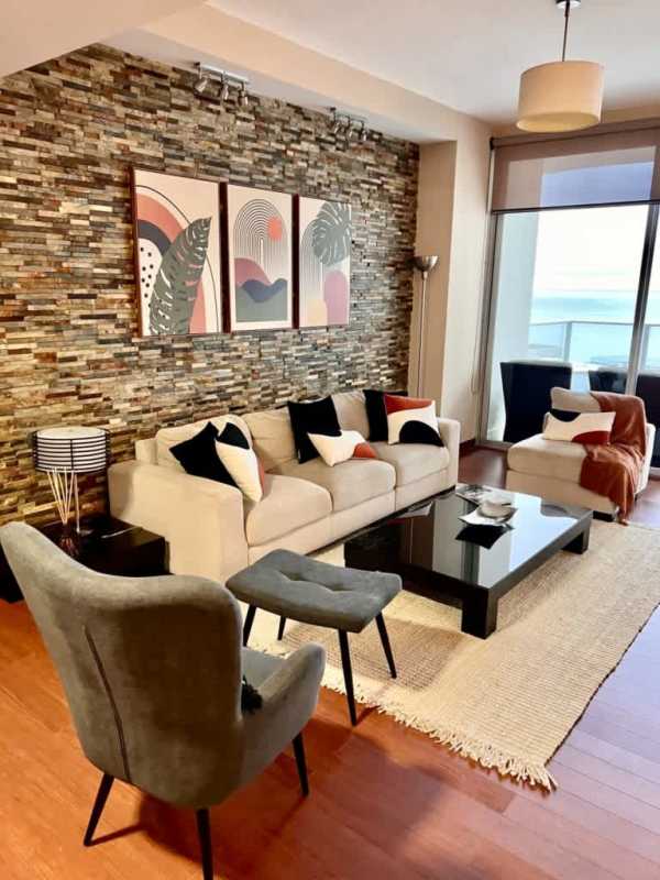 Living room with floor-to-ceiling windows, stone accent wall, neutral decor and ocean view at PH Ocean Club Punta Pacifica