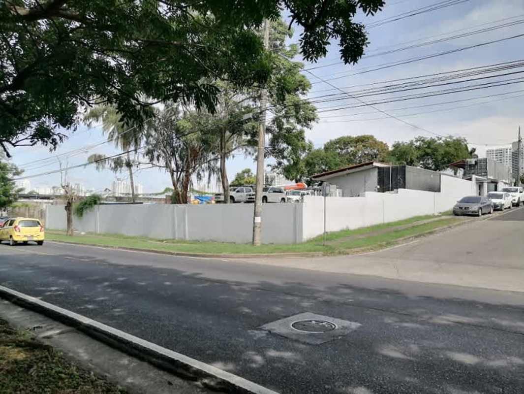 Vacant gravel lot with patches of grass and boundary fence along main road in Parque Lefevre