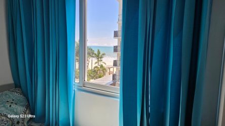 Bedroom featuring blue curtains, window with partial ocean view, bright natural lighting at PH Ventanas del Mar Playa Caracol Panama