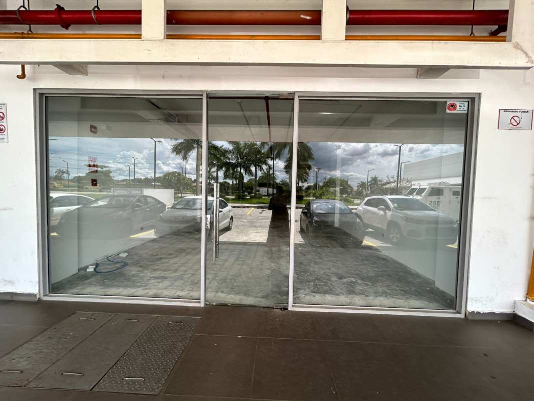 Glass storefront entrance reflecting parking lot and palm trees in La Siesta Tocumen Panama