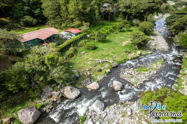 Aerial of country house beside Chiriquí Viejo River with lush forest backdrop in Paso Ancho