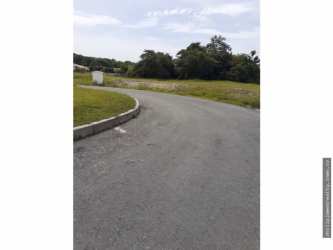 Open plot with boundary fence and red-roof house nearby at Hacienda Pacífica