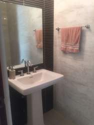 Bright modern bathroom with pedestal sink, large mirror, tiled walls River Valley Panama Pacifico