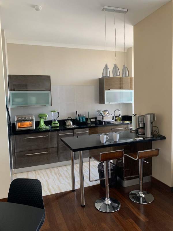 Open kitchen with island seating, pendant lighting, black granite counters in Denovo Tower apartment Panama