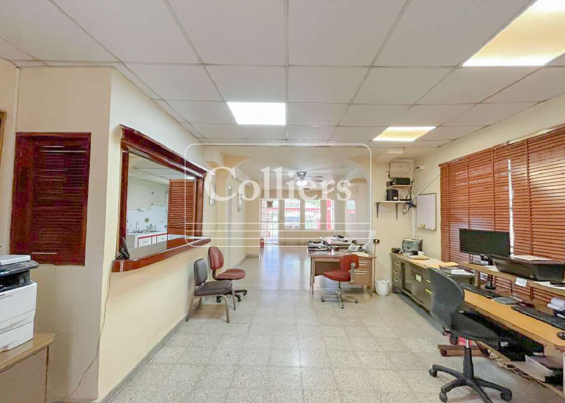 Office interior with reception window, multiple desks, and blinds in commercial building