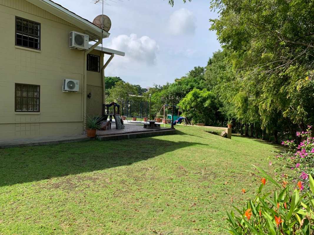 Green backyard with lawn, children playground, shaded patio of family house Clayton Panama