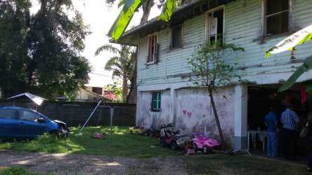 Weathered two-story structure with fence and green yard central Colón City Panama