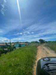 Rural dirt road with grassy surroundings, homes and bright sky in Playa Leona Capira