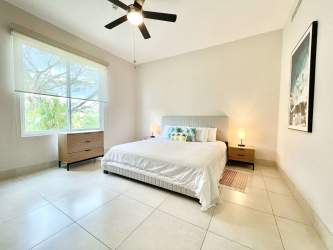 Spacious bedroom with large window, king bed, ceiling fan, neutral decor, overlooking tropical gardens