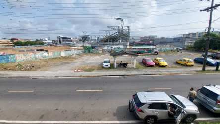 City skyline visible across vacant commercial lot in downtown Colon Panama with cars and transit access