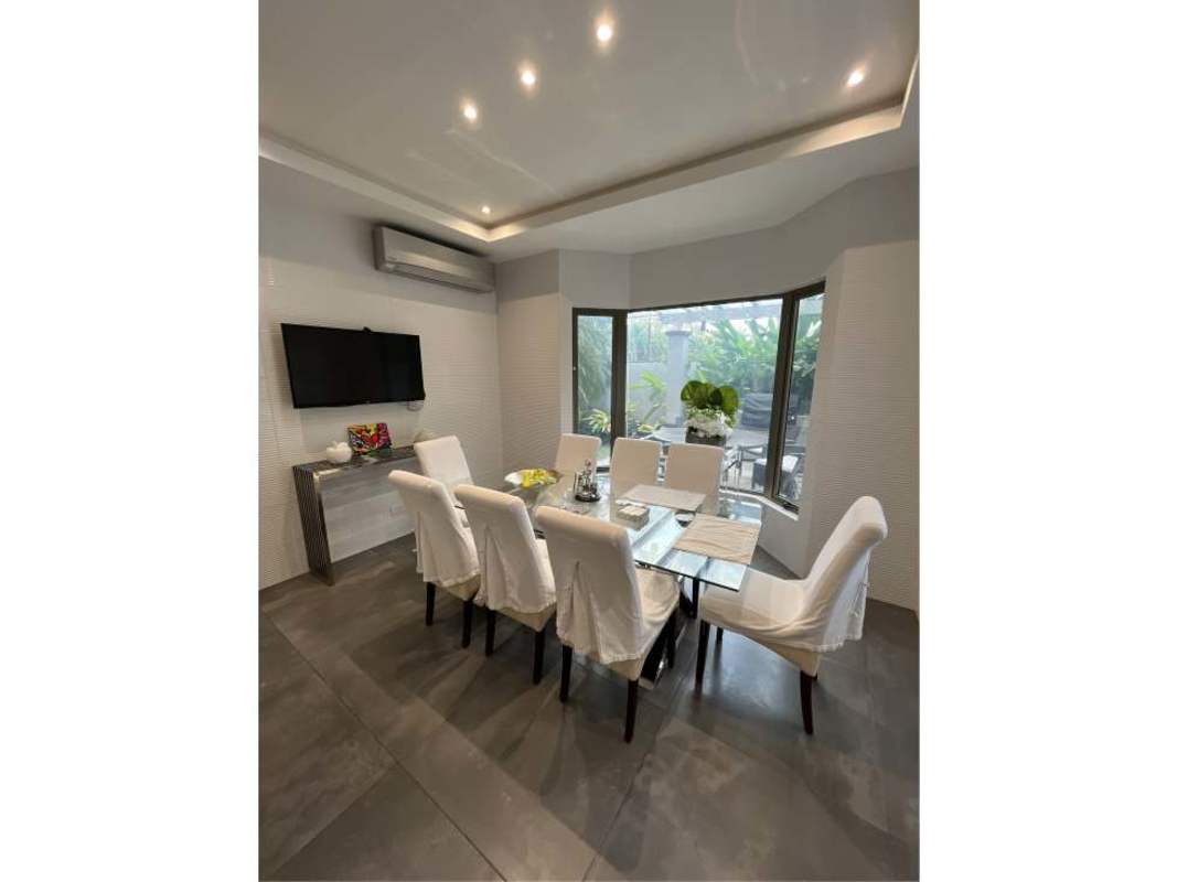 Bright dining area with glass table, bay window, wall TV in luxury Costa del Este house Panama City