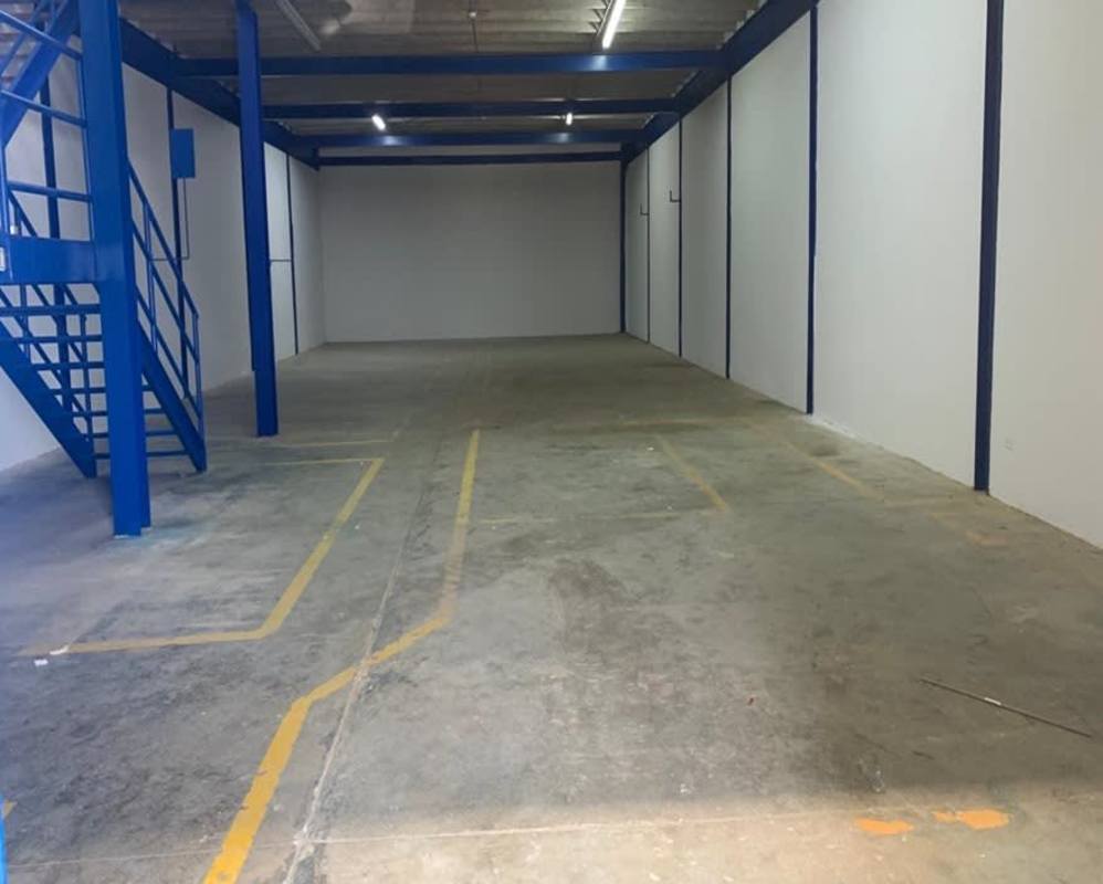 Spacious empty warehouse with blue steel staircase, marked floor, and white walls in Los Pueblos Panama