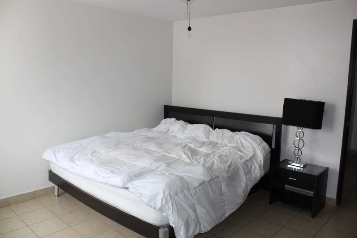 Minimal modern bedroom with tile floor, white bedding and black furniture in Obarrio Plaza Panama apartment