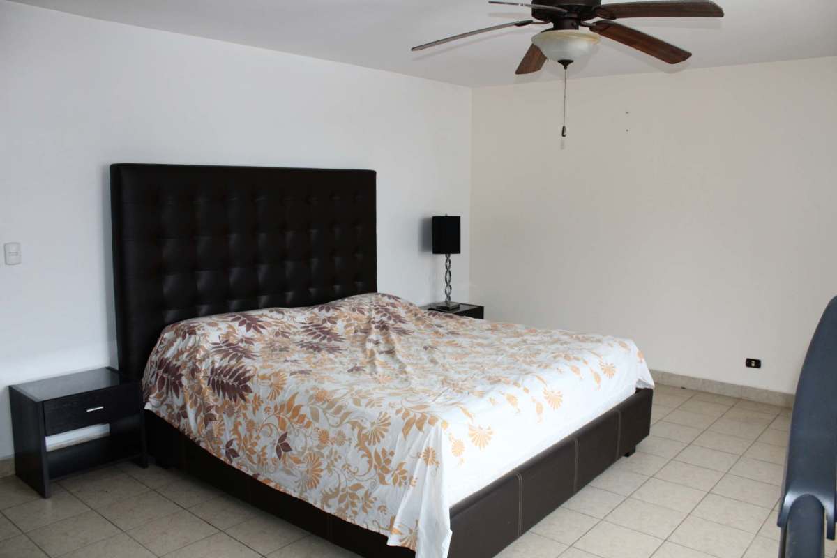 Spacious master bedroom with large tufted headboard, tile floor, fan at Obarrio Plaza Panama apartment