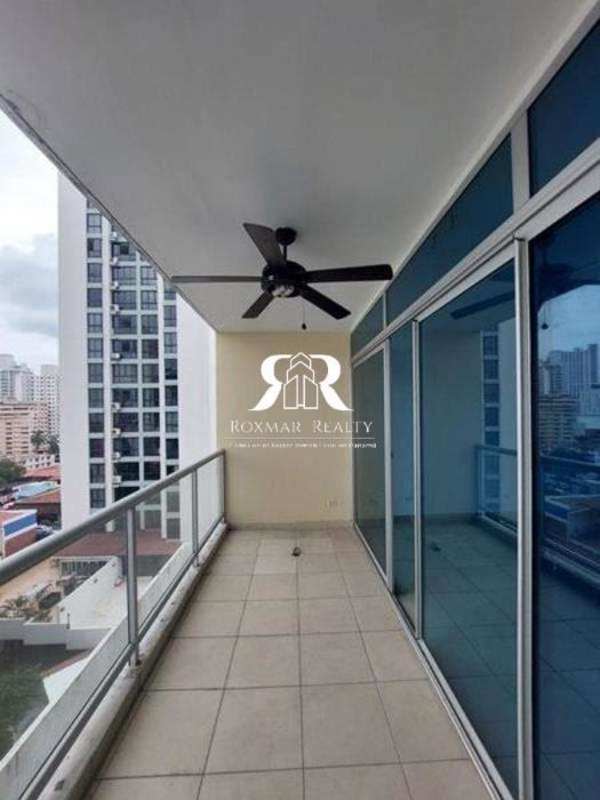 Spacious balcony with glass railings, ceiling fan, tile flooring, and Panama City skyline view in PH El Cangrejo Suites
