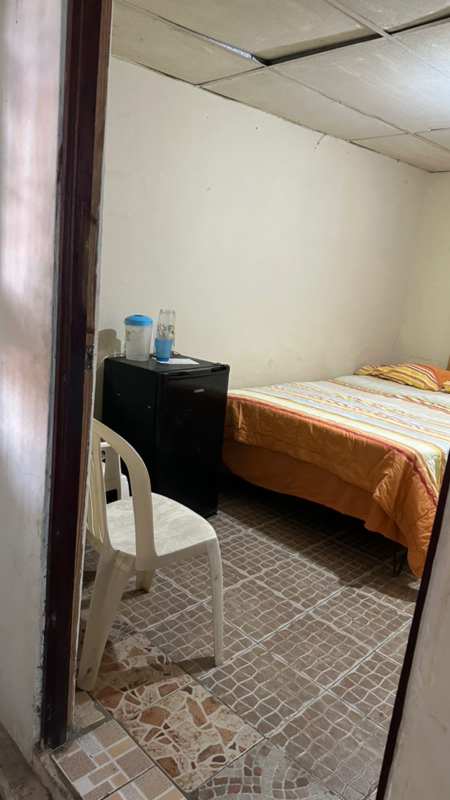 Simple bedroom with bed, fridge, plastic chair, basic furnishing in Pedregal Panama City