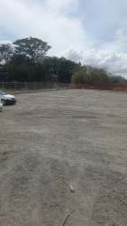 Open fenced gravel lot with vegetation and car view, ideal retail development site in Arraiján Panama