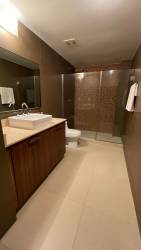 Modern bathroom with glass shower, wood cabinet, and bright lighting in PH River Valley Howard Panama