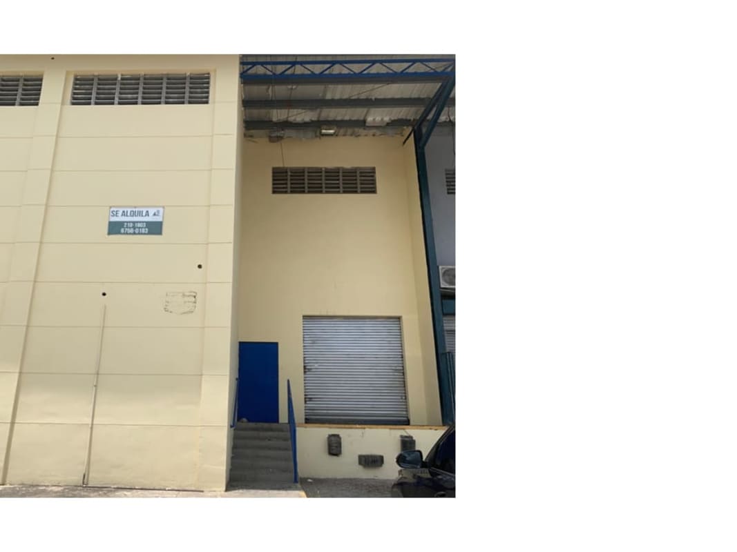 Exterior of beige industrial warehouse with metal roll-up door and security gate Llano Bonito Panama