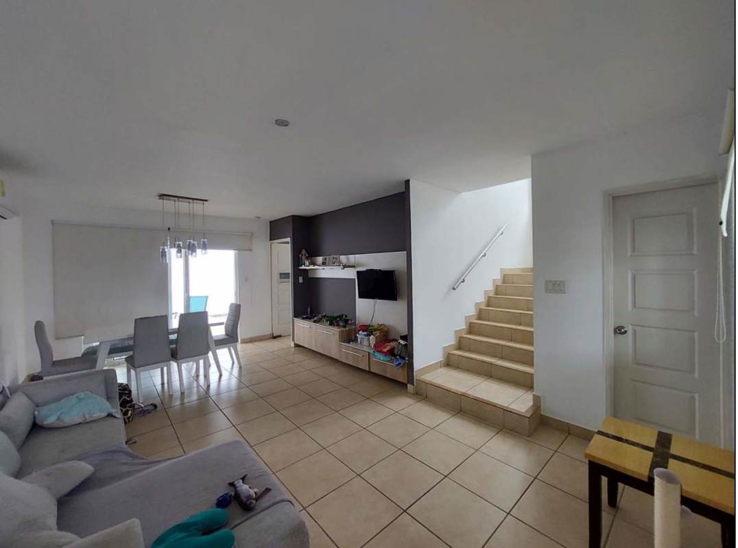 Open concept living dining area with gray sofa, staircase and accent wall in duplex Panama
