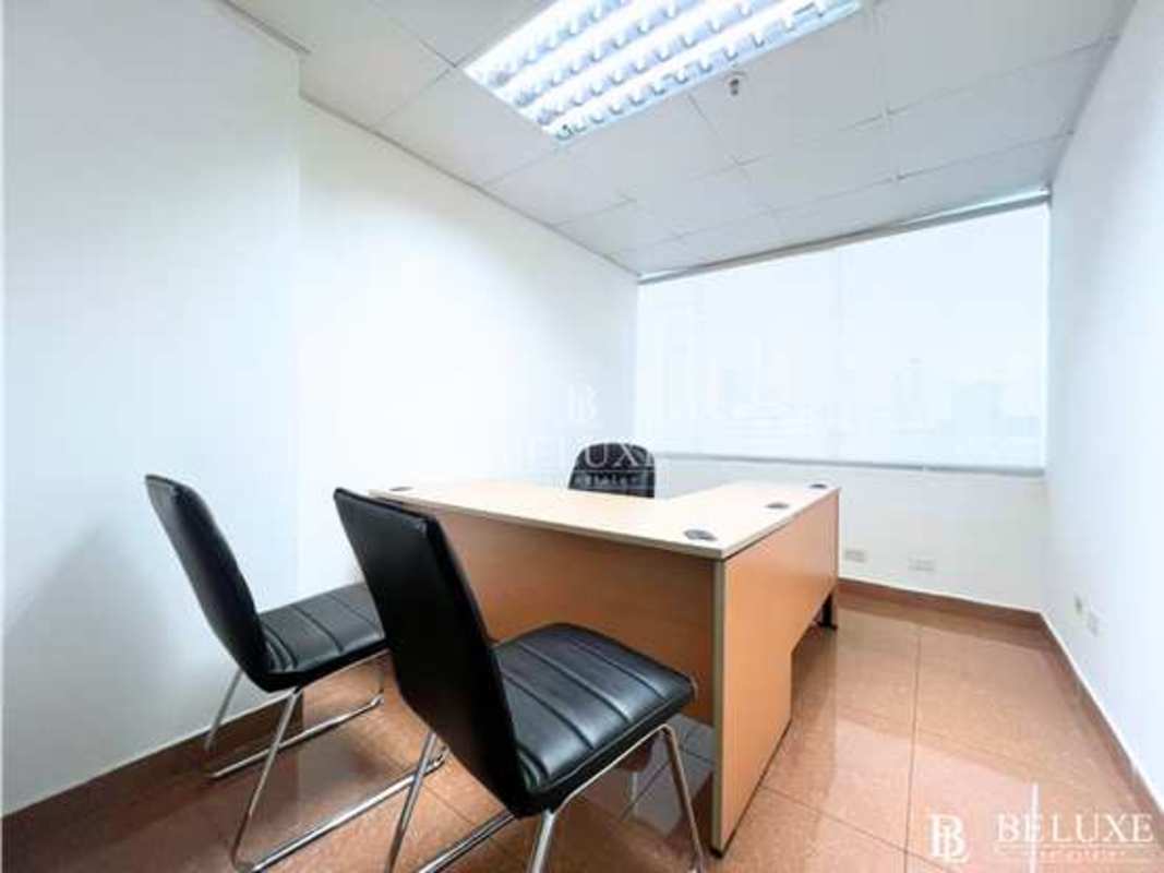 Open-plan work area in commercial office with tiled flooring, windows with blinds, and fluorescent lighting