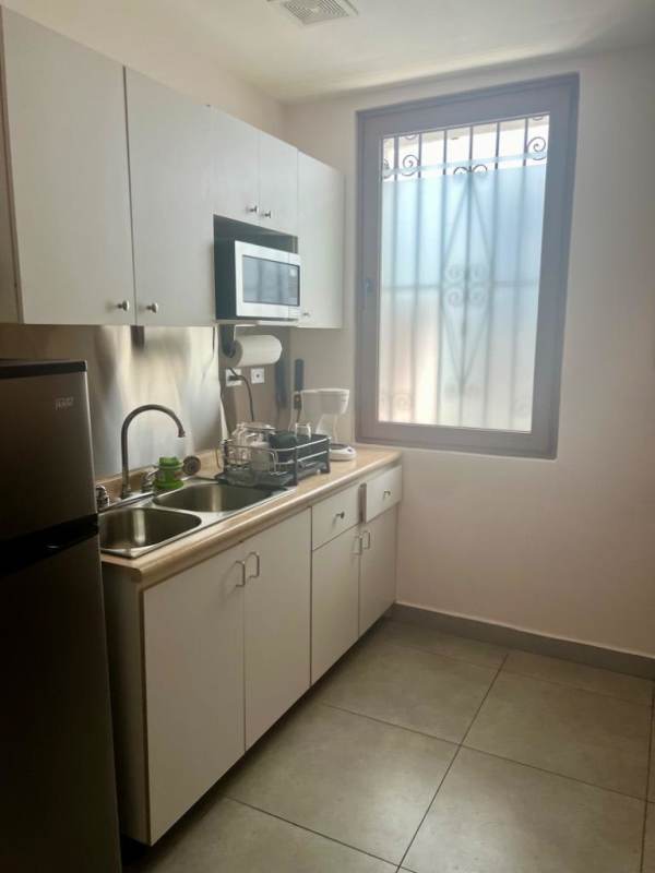 Compact kitchenette with white cabinets, microwave space, sink in commercial office Panama City