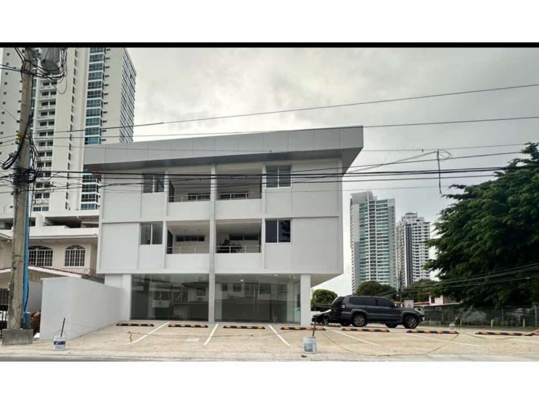 Three-story modern commercial building with large windows, balconies, parking area in urban Panama City San Francisco