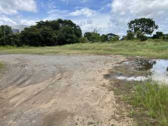 Vacant open lot with gravel, greenery, puddle, trees surrounding, under blue sky in David Chiriquí Panama