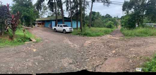 Wide angle of mixed-use property corner lot with trees gravel access and storefronts Altos de San Francisco