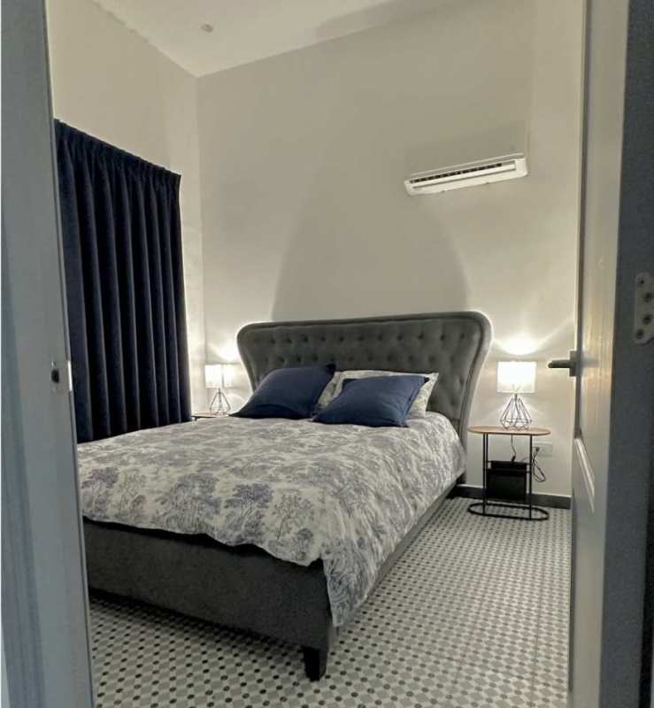 Bright bedroom with upholstered bed, AC unit, traditional tile floor in Casco Viejo apartment Panama